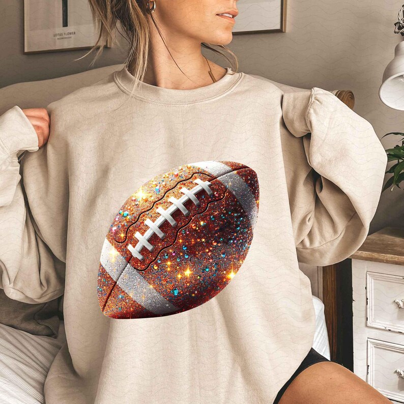 May include: A beige sweatshirt with a glittery brown football design.
