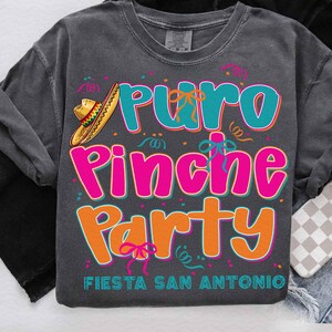 May include: A gray t-shirt with the text "Puro Pinche Party Fiesta San Antonio" in colorful letters. The text is surrounded by confetti and a sombrero.