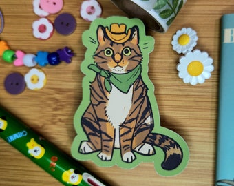 Peut inclure: Un chat tabby brun et blanc portant un bandana vert et un chapeau de cowboy brun. Le chat est assis sur un fond vert.