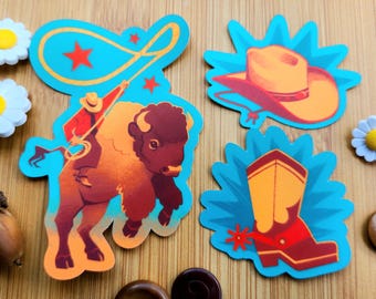 Peut inclure: Quatre autocollants colorés sur le thème du Far West. L'un représente un cow-boy sur un bison avec un lasso. Les autres montrent un chapeau de cow-boy, une botte de cow-boy avec un éperon et une étoile. Les autocollants sont sur une surface en bois.