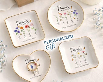 May include: Four white ceramic trinket dishes with gold rims, each featuring a floral design and the text "Nana's Garden." One heart-shaped dish holds a ring. The phrase "Love Grows Here" is also present. The word "Personalized Gift" is also visible.