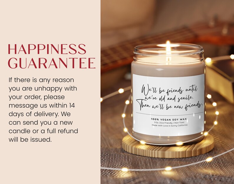 a candle on a wooden stand with a string of lights around it. The candle has a label that reads "Happiness Guarantee" and "We'll be friends until we're old and sick. Then we'll be new friends." The candle is placed on a table with a blurred background.