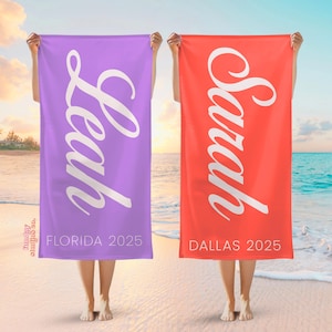 Puede incluir: Dos toallas de playa personalizadas, una lavanda y otra coral, se sostienen frente a un fondo de playa. La toalla lavanda tiene el nombre "Leah" y "Florida 2025". La toalla coral tiene el nombre "Sarah" y "Dallas 2025".