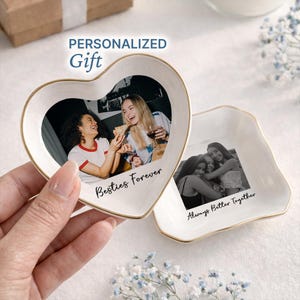May include: Two white ceramic trinket dishes, one heart-shaped and one square, with gold rims. The heart-shaped dish has a photo of two women and the text "Besties Forever." The square dish has a photo of three women and the text "Always Better Together." The words "PERSONALIZED Gift" are above the heart-shaped dish.