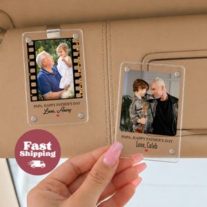 May include: Two clear acrylic photo frames with pictures of a grandfather and child. The frames are attached to a car visor. Text on the frames reads "PAPA, HAPPY FATHER'S DAY" and "Love, Avery" and "Love, Caleb".