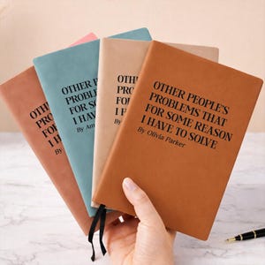 May include: A set of four rectangular notebooks in tan, teal, beige, and brown with black text on the covers reading OTHER PEOPLE'S PROBLEMS THAT FOR SOME REASON I HAVE TO SOLVE. Each notebook cover includes a line for the author's name.