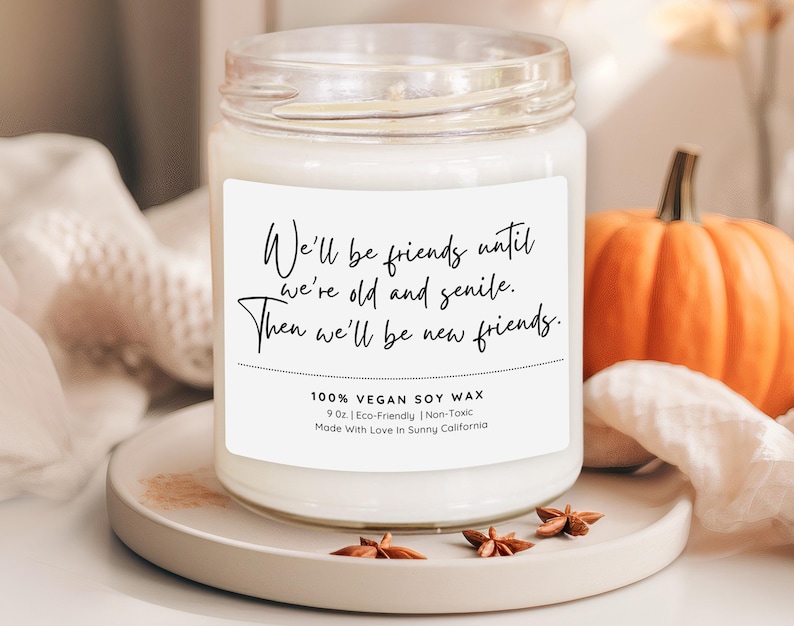 a white candle with a label that reads "We'll be friends until we're old and gentle. Then we'll be new friends." The candle is placed on a white plate, with a small orange pumpkin and some star anise nearby.