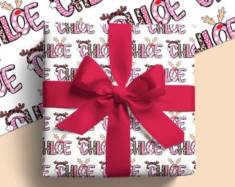 May include: A present wrapped in white paper printed with the name "Chloe" in pink and brown, adorned with reindeer antlers. The gift is tied with a bright red ribbon and bow. The overall theme is festive.