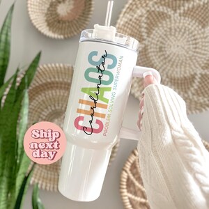 Puede incluir: Vaso blanco con asa y tapa transparente. El vaso tiene las palabras "Chaos Coordinator Problem Solving Superwoman" en texto colorido. Una pajita transparente est&aacute; insertada en la tapa. El vaso lo sostiene una persona que lleva un su&eacute;ter blanco.