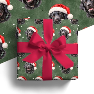 Pode incluir: Uma caixa de presente quadrada embrulhada em papel verde escuro com um padrão repetitivo de cães Labrador pretos usando gorros de Papai Noel vermelhos e brancos, acentuado com flocos de neve brancos. Um grande laço vermelho está amarrado.