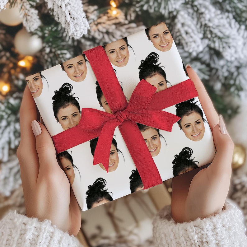 May include: A wrapped gift with a white background covered in smiling faces. The gift is wrapped with a red bow. The gift is held by a person wearing a white sweater.