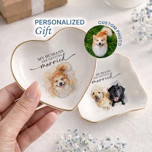May include: Two white heart-shaped ceramic trinket dishes with gold-painted rims. One dish features a watercolor illustration of a corgi and the text MY HUMANS ARE GETTING married. The other dish shows a golden retriever and a black labrador.