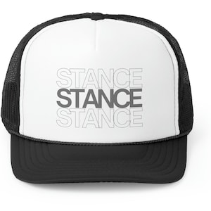 Puede incluir: Una gorra de camionero blanca con una malla negra en la parte posterior. La parte delantera de la gorra tiene la palabra "STANCE" escrita tres veces en formato apilado, con cada palabra contorneada en blanco.