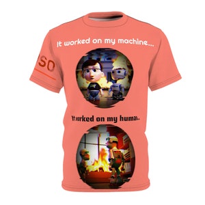 May include: Coral-colored t-shirt featuring a cartoon illustration of a person and a robot in a fiery setting. The text "It worked on my machine..." and "It worked on my human..." are printed above and below the illustration. The word "SO" is printed on the sleeve.