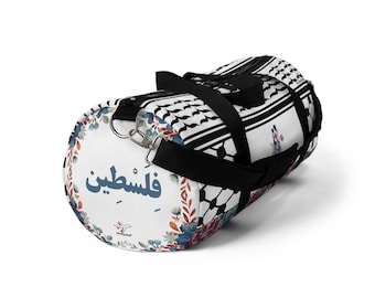 Könnte beinhalten: Zylindrische Sporttasche mit weißem Hintergrund. Die Tasche hat ein schwarz-weißes Muster, florale Akzente und das Wort "فلسطين" in Blau. Schwarze Träger und silberne Metallringe sind angebracht.