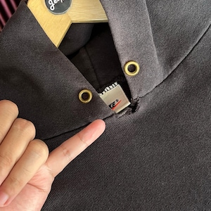 May include: Close-up of a dark gray hoodie with a drawstring hood and gold-colored eyelets. The Nike brand label is visible at the neckline. The hoodie is hanging on a wooden hanger.