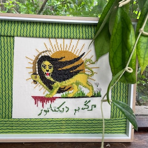 May include: Framed cross-stitch artwork featuring a lion with a sunburst background. The lion is yellow and black, holding a sword. The artwork includes green and white borders and text in a foreign language.