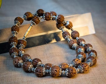 May include: A double-strand bracelet featuring intricately carved brown beads with silver-colored accents. The beads have a detailed, textured surface. The bracelet is displayed on a neutral-toned surface, showcasing the craftsmanship of the jewelry.