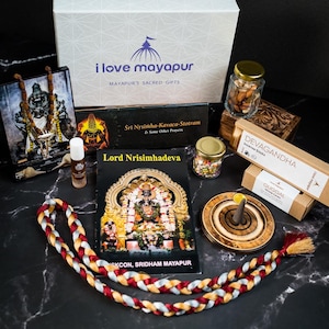 May include: A gift box filled with items for a spiritual practice. The box includes a book titled "Lord Nrisimhadeva", a small framed image of a deity, a bottle of oil, a string of beads, incense sticks, a wooden incense burner, a small bag of dried fruit, and a small book titled "Śri Nrsimha-Kavaca-Stotram & Some Other Prayers".