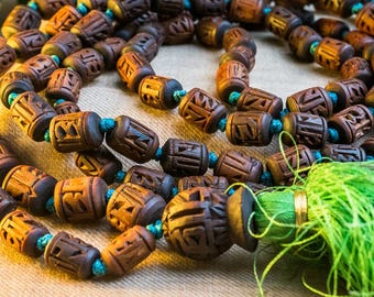 May include: A brown wooden mala bead necklace with a green tassel. The beads are carved with intricate designs and are strung on a blue cord.