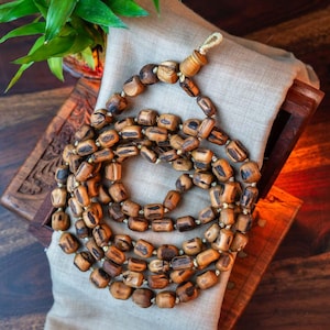 May include: A long strand of wooden beads, with a dark brown and light brown striped pattern, is coiled on a beige fabric surface. The beads are strung together with a thin, light brown cord.