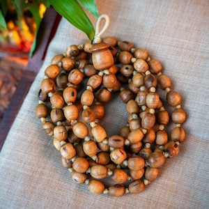 Può includere: Una collana di mala di legno con un fiocco marrone. Le perle sono infilate su un cordoncino in fibra naturale. Il mala è una collana di preghiera tradizionale indù.