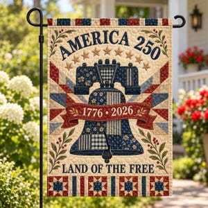 Puede incluir: Una bandera de jardín rectangular con un diseño acolchado y una campana central. El texto dice AMERICA 250, 1776-2026 y LAND OF THE FREE. La paleta de colores incluye crema, azul marino y rojo con patrones de estrellas y flores.