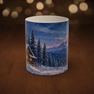 May include: A white ceramic mug featuring a printed winter landscape scene. The image displays a snow-covered cabin with glowing yellow windows nestled among tall pine trees, set against a backdrop of blue mountains under a snowy sky.