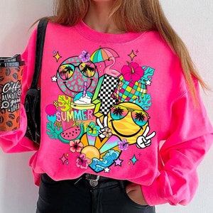 Peut inclure: Sweat-shirt rose avec un imprim&eacute; graphique color&eacute; repr&eacute;sentant des visages souriants, des palmiers, des lunettes de soleil, une past&egrave;que, un flamant rose et le texte "Summer Vibes".