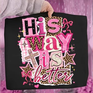 May include: Black tote bag with the text "His Way is Better" in pink, leopard print, and gingham patterns. The design includes a cross, stars, and bows. The bag is held by a person.