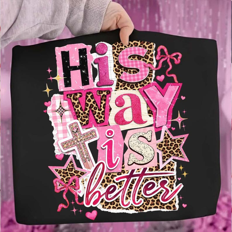 May include: Black tote bag with the text "His Way is Better" in pink, leopard print, and gingham patterns. The design includes a cross, stars, and bows. The bag is held by a person.