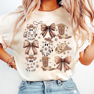 May include: A cream-colored t-shirt with a graphic print of various cowboy-themed ghosts, boots, and bows in brown and white. The design features a repeating pattern of these elements.