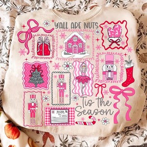May include: Beige sweatshirt with a festive design featuring pink and red Christmas-themed illustrations. The design includes a gingerbread house, nutcrackers, a Christmas tree, and the text "Y'all Are Nuts" and "Tis the Season".