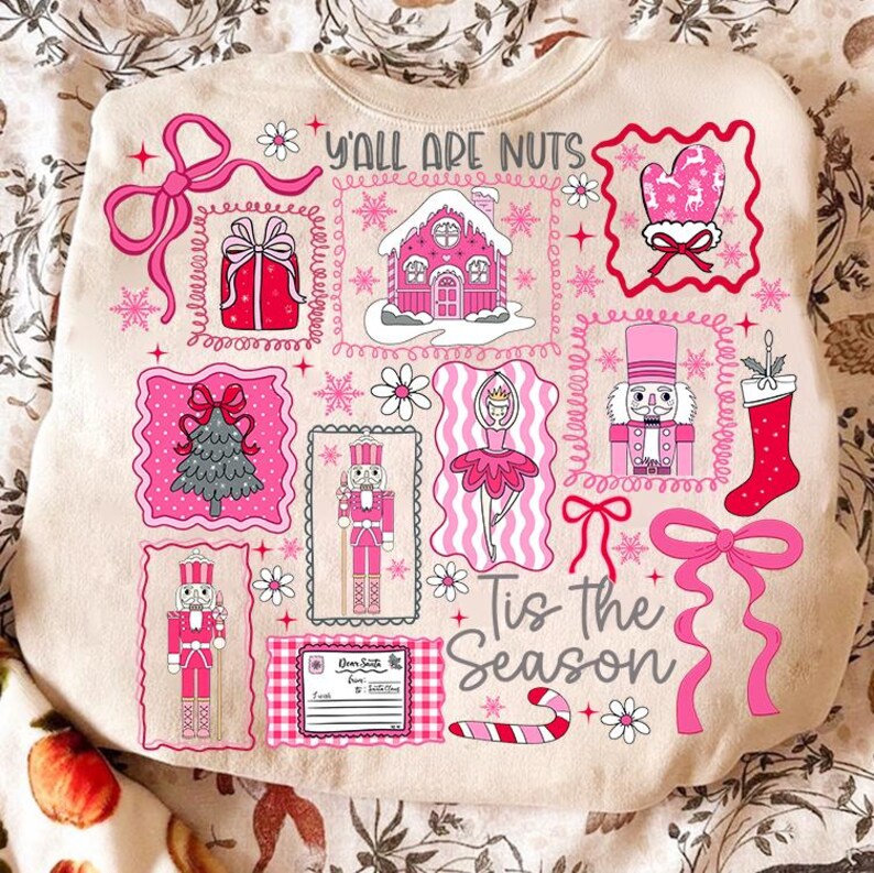 May include: Beige sweatshirt with a festive design featuring pink and red Christmas-themed illustrations. The design includes a gingerbread house, nutcrackers, a Christmas tree, and the text "Y'all Are Nuts" and "Tis the Season".