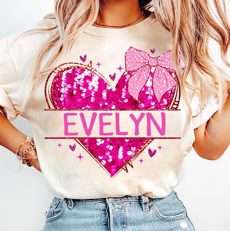 May include: A white t-shirt with a pink sequined heart and a pink bow. The heart has the name "EVELYN" written across it.