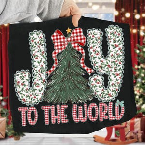 May include: Black Christmas cushion featuring the phrase "JOY TO THE WORLD". The letters are decorated with a floral pattern, and a red and white checked bow. A green Christmas tree is in the center of the design.