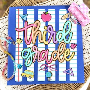 Peut inclure: T-shirt bleu avec un motif color&eacute; "troisi&egrave;me ann&eacute;e". Le design comprend un avion en papier, une pomme, un crayon, des fleurs, un bus scolaire, un n&oelig;ud, un globe et un triangle. Un collier de perles et une pince &agrave; cheveux rose sont &eacute;galement visibles.