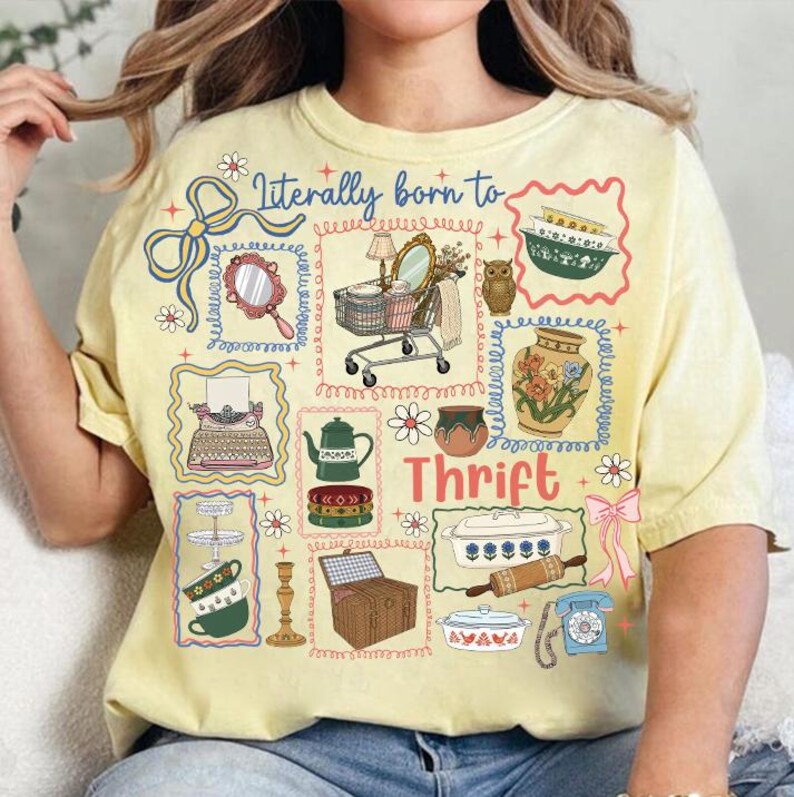 May include: Yellow t-shirt with a colorful graphic design featuring the text "Literally born to Thrift." The design includes illustrations of vintage items like a typewriter, mirror, and shopping cart.