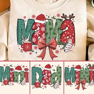 May include: A set of three Christmas-themed sweatshirts with the words "Mama", "Mini Dad", and "Mini" in festive red, green, and white colors. Each design features a Santa hat, a bow, a cup of hot cocoa, and a Christmas tree.