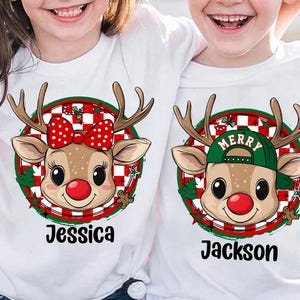 May include: White t-shirts with cartoon reindeer faces, antlers, red noses, and festive details. One reindeer has a red bow, the other a green cap with "MERRY". Names "Jessica" and "Jackson" are printed below.