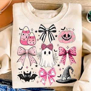 May include: A cream-colored sweatshirt with a pink and black Halloween-themed design. The design features candy corn, bows, a ghost, a witch's hat, and a pumpkin.