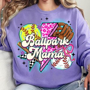 Puede incluir: Una sudadera lila con un gr&aacute;fico tem&aacute;tico de b&eacute;isbol. El dise&ntilde;o incluye una pelota de b&eacute;isbol, un guante, un bate y el texto "Ballpark Mama" en una fuente retro. El gr&aacute;fico incorpora estampado de leopardo rosa y acentos de estrella.