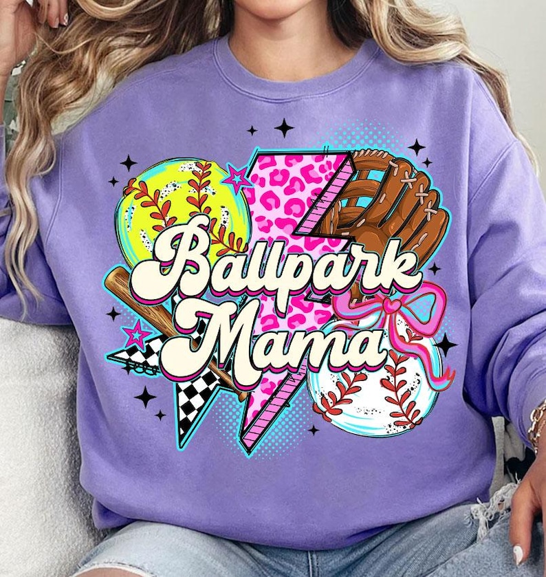 Puede incluir: Una sudadera lila con un gr&aacute;fico tem&aacute;tico de b&eacute;isbol. El dise&ntilde;o incluye una pelota de b&eacute;isbol, un guante, un bate y el texto "Ballpark Mama" en una fuente retro. El gr&aacute;fico incorpora estampado de leopardo rosa y acentos de estrella.