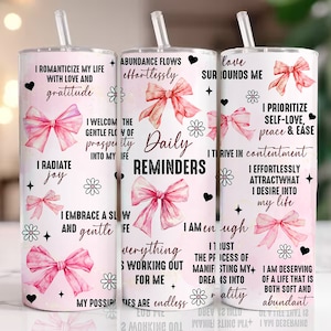 May include: Two pink and white tumblers with inspirational quotes and pink bows. The quotes include "I romanticize my life with love and gratitude", "Daily Reminders", "Love surrounds me", "I prioritize self-love, peace & ease", "I am enough", and "I am deserving of a life that is both soft and abundant".