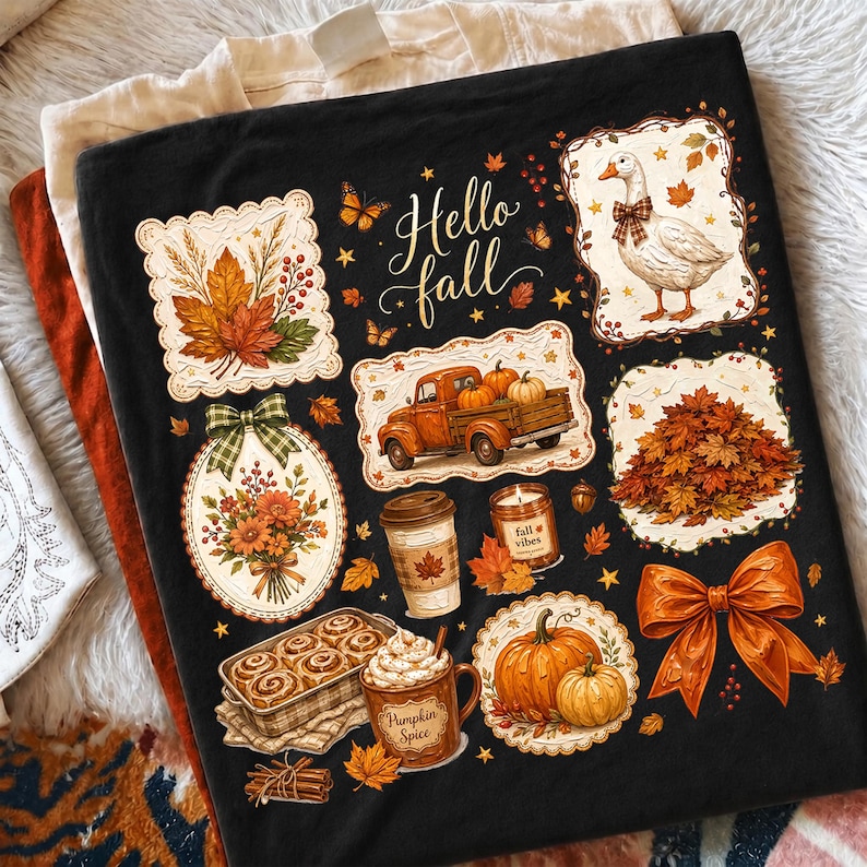 K&ouml;nnte beinhalten: Ein schwarzes T-Shirt mit dem Text Hello fall und verschiedenen herbstlichen Illustrationen, darunter eine Gans mit Schleife, ein Lastwagen mit K&uuml;rbissen, ein Blumenstrau&szlig;, eine Kaffeetasse, eine Kerze, Zimtschnecken und eine gro&szlig;e orangefarbene Schleife.