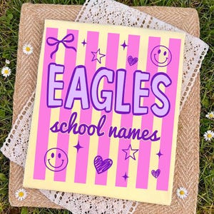 Op de afbeelding: Een rechthoekig canvas met een geel en roze gestreepte achtergrond. Het canvas toont het woord "EAGLES" in paars, samen met de woorden "school names". Het ontwerp bevat harten, sterren, een strik en smiley gezichten.