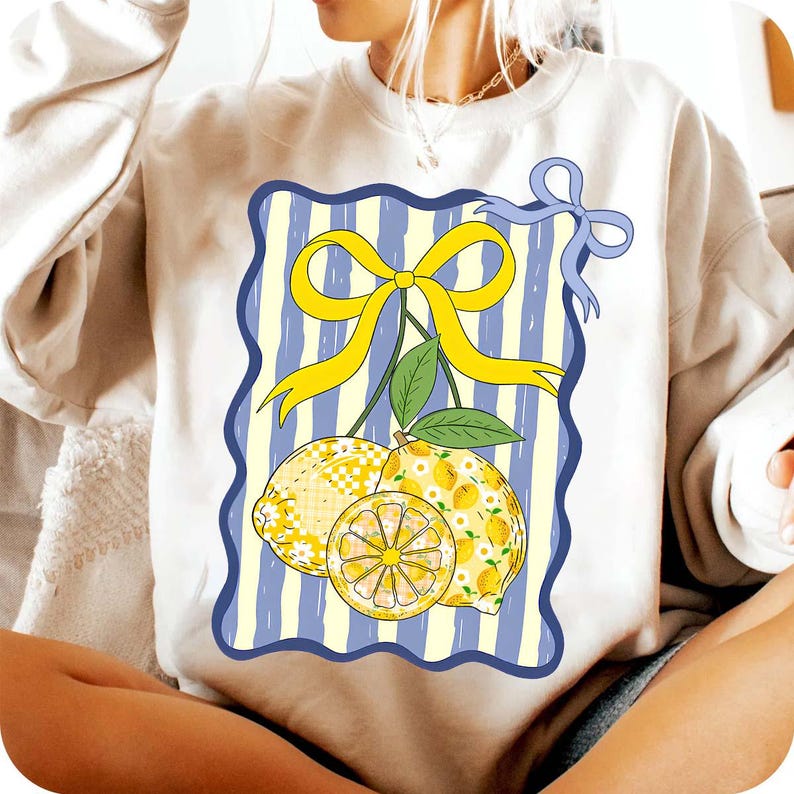 Pu&ograve; includere: Una felpa bianca con una grafica di limoni e un fiocco giallo su uno sfondo a righe blu e bianco.