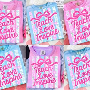 May include: A collection of six t-shirts in various pastel colors, including pink, blue, and purple. Each shirt features the text "Teach Love Inspire" in a pink, glittery font, with a bow design above the text. The shirts are displayed on a light background.