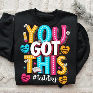 May include: Black sweatshirt with a colorful graphic that says "You Got This" with a book, pencil, and hearts. The text "#testday" is below the graphic.
