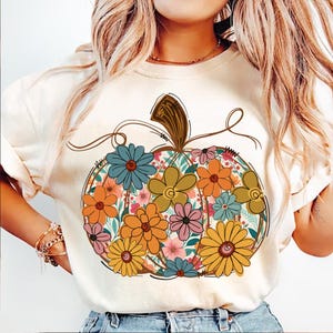 May include: Cream-coloured sweatshirt with a floral pumpkin design. The pumpkin is filled with colourful flowers in shades of orange, blue, yellow, and pink. The design has a vintage, retro style, perfect for autumn.